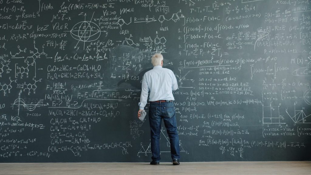 Man writing complex formulas on a chalkboard wall